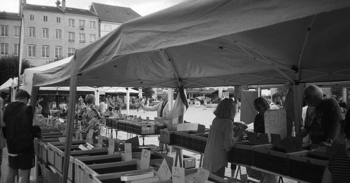 Photo en noir et blanc d'une scène de marché animé à Nancy, France, avec des stands de livres et des personnes qui feuillettent.