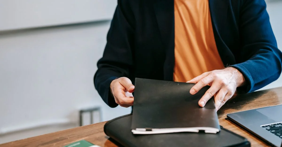 Un professionnel en costume blazer organise des documents sur un bureau en bois dans un bureau.