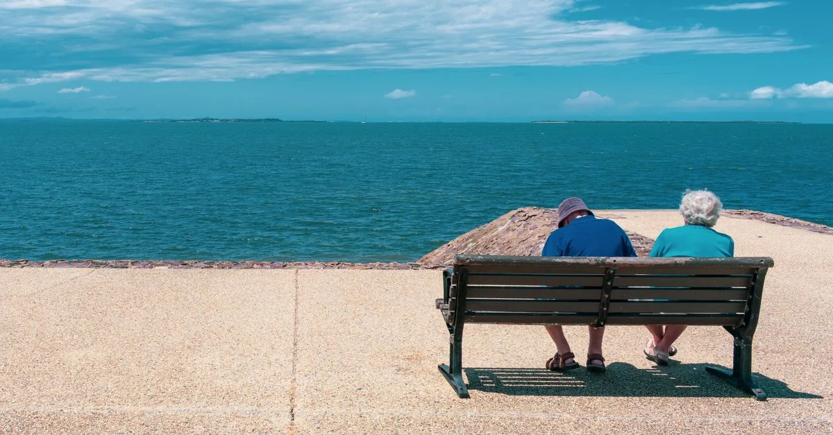 Couple senior se relaxant sur un banc en bord de mer, profitant d'une journée d'été ensoleillée avec vue sur l'océan.