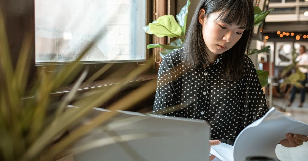 Femme asiatique travaillant intensément sur des documents à son ordinateur portable dans un bureau moderne.