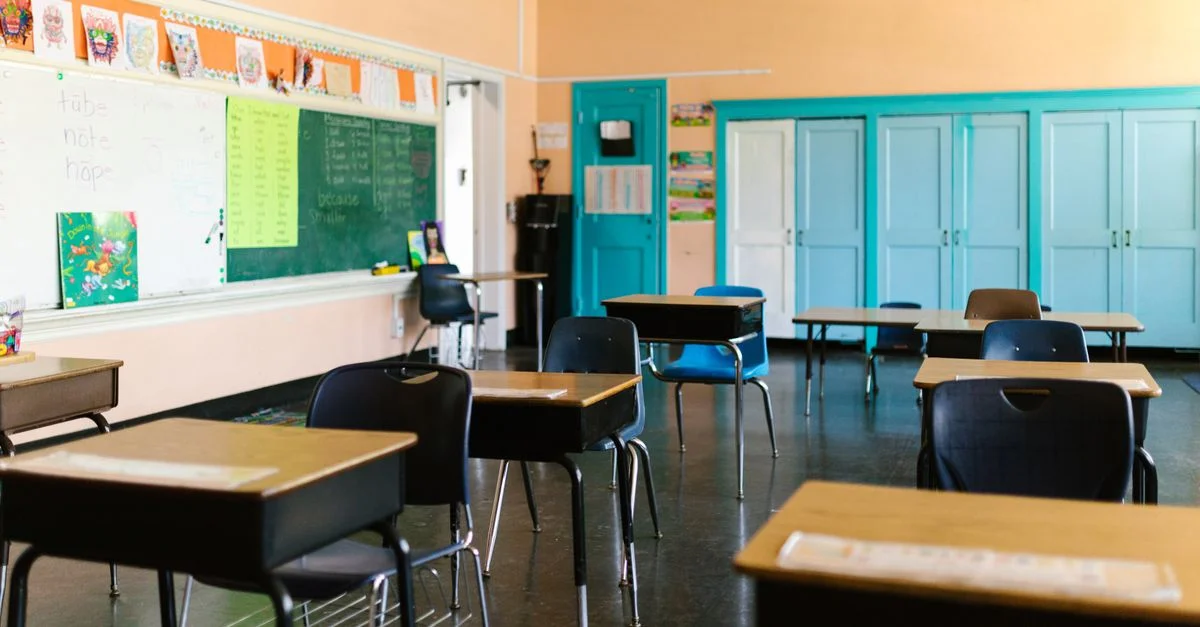 Salle de classe vide, lumineuse et colorée avec des bureaux, un tableau noir et des matériaux éducatifs.
