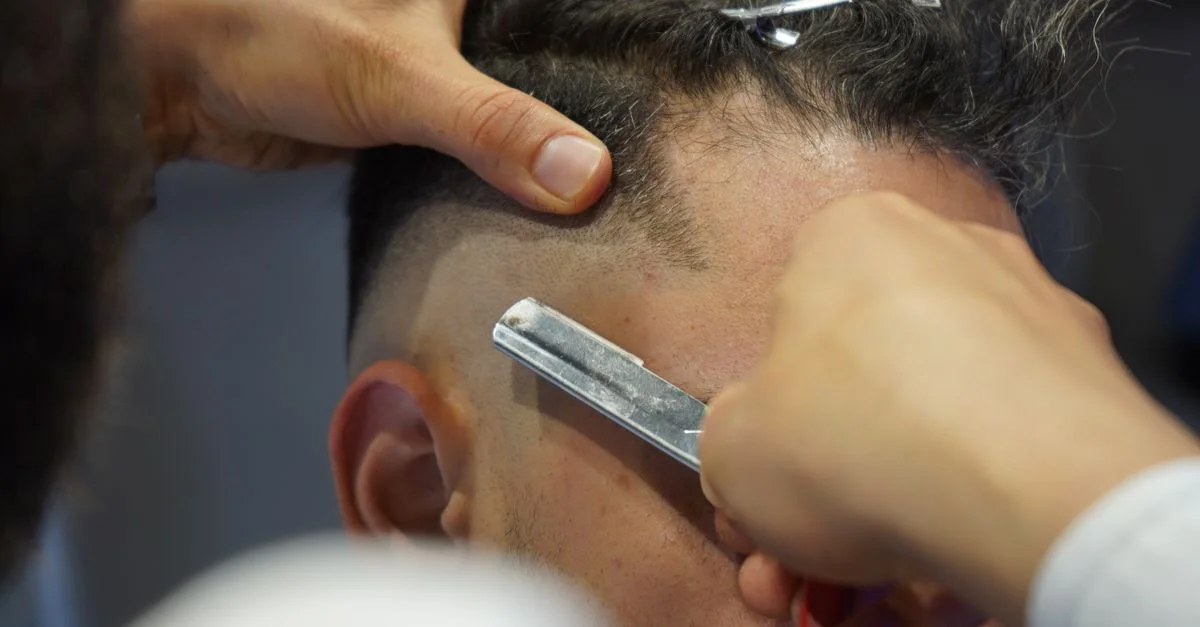 Gros plan sur un barbier utilisant habilement une lame de rasoir pour une coupe de cheveux dégradée précise sur un client.