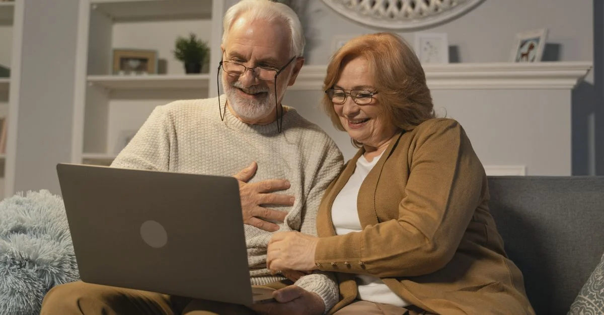 Couple senior heureux assis sur un canapé ayant un appel vidéo joyeux sur un ordinateur portable dans un salon confortable.