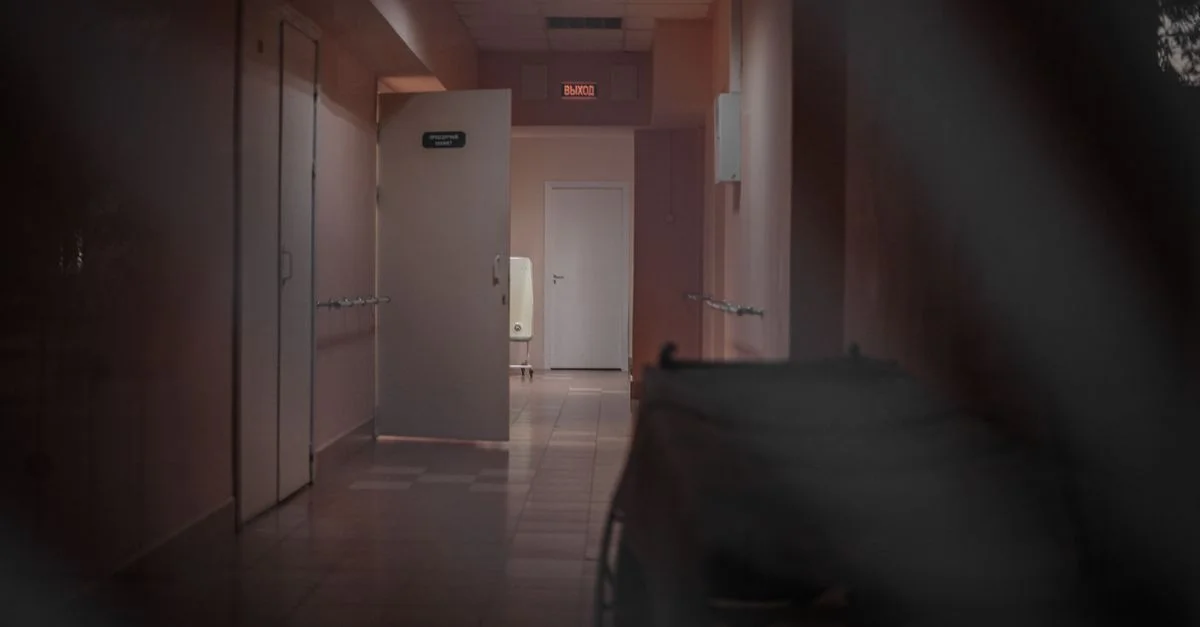 Un couloir d'hôpital désert avec des portes ouvertes et un éclairage tamisé, renforçant une ambiance mystérieuse.