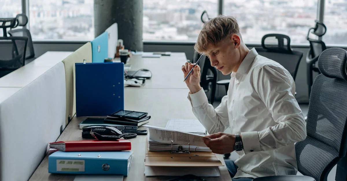 Homme en chemise blanche concentré sur des papiers à un bureau moderne avec vue sur la ville.