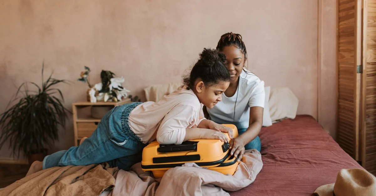 Une mère et sa fille préparent une valise jaune dans une chambre chaleureuse.